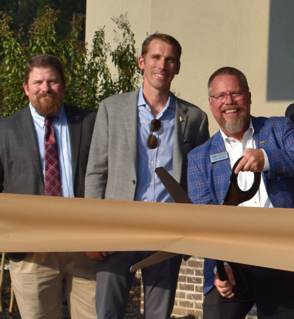 Three men in suits at an outdoor ribbon-cutting ceremony.