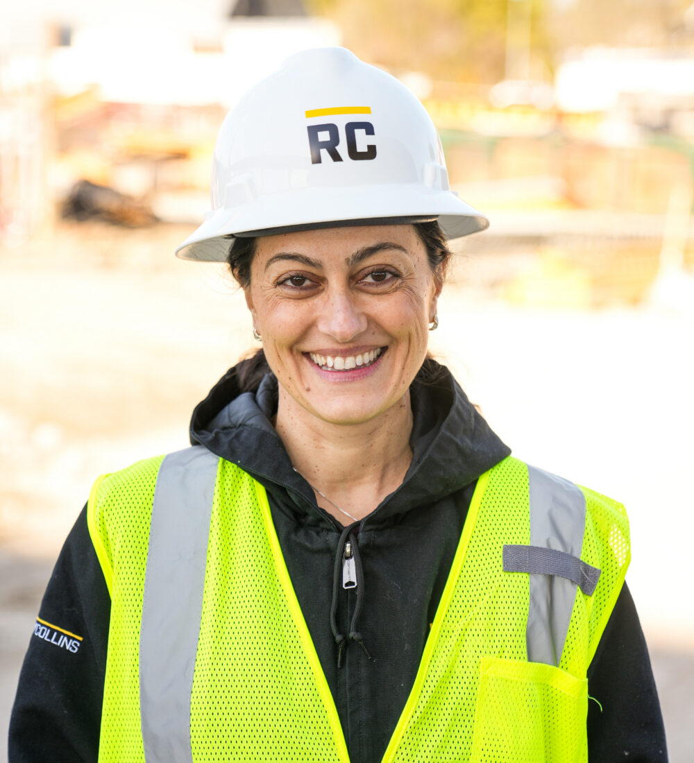 Woman in RC hard hat and yellow vest smiling at site.