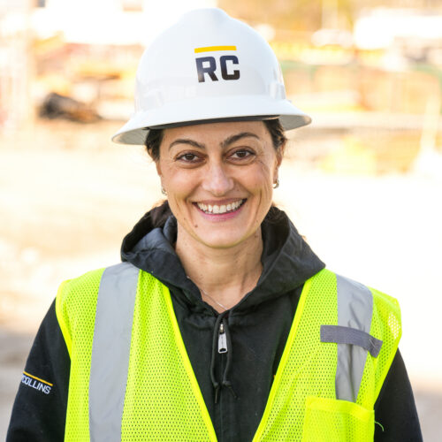 Woman in RC hard hat and yellow vest smiling at site.