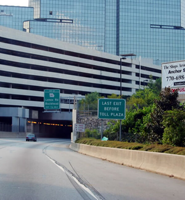 Car approaches tunnel under parking garage, passing green exit signs.