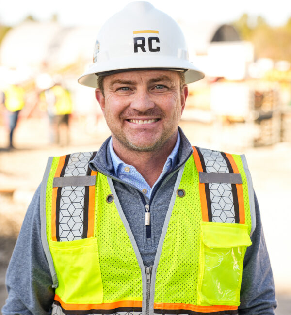 Smiling worker in RC hard hat and neon vest at site.