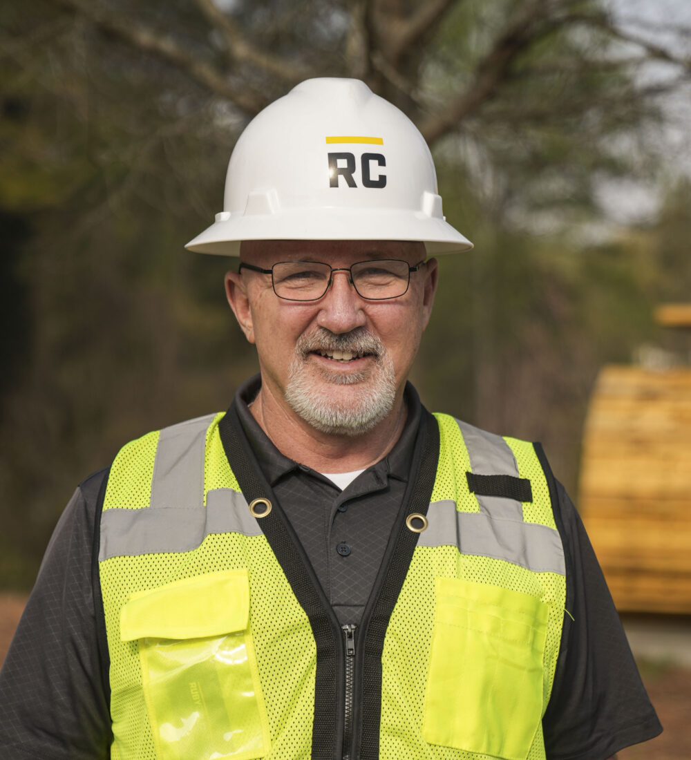 Smiling man in hard hat and safety vest at construction site.